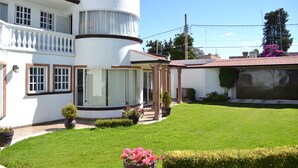 A white building with a balcony, a covered porch, and a well-maintained lawn with potted plants. - Hotel La Aurora (Huamantla)