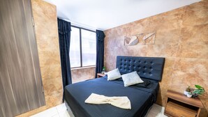 A bedroom with a large bed, a wooden nightstand, a potted plant, and a window with curtains. - 5 Bedroom - 1 Block from Lleras - P2 (Medellín)