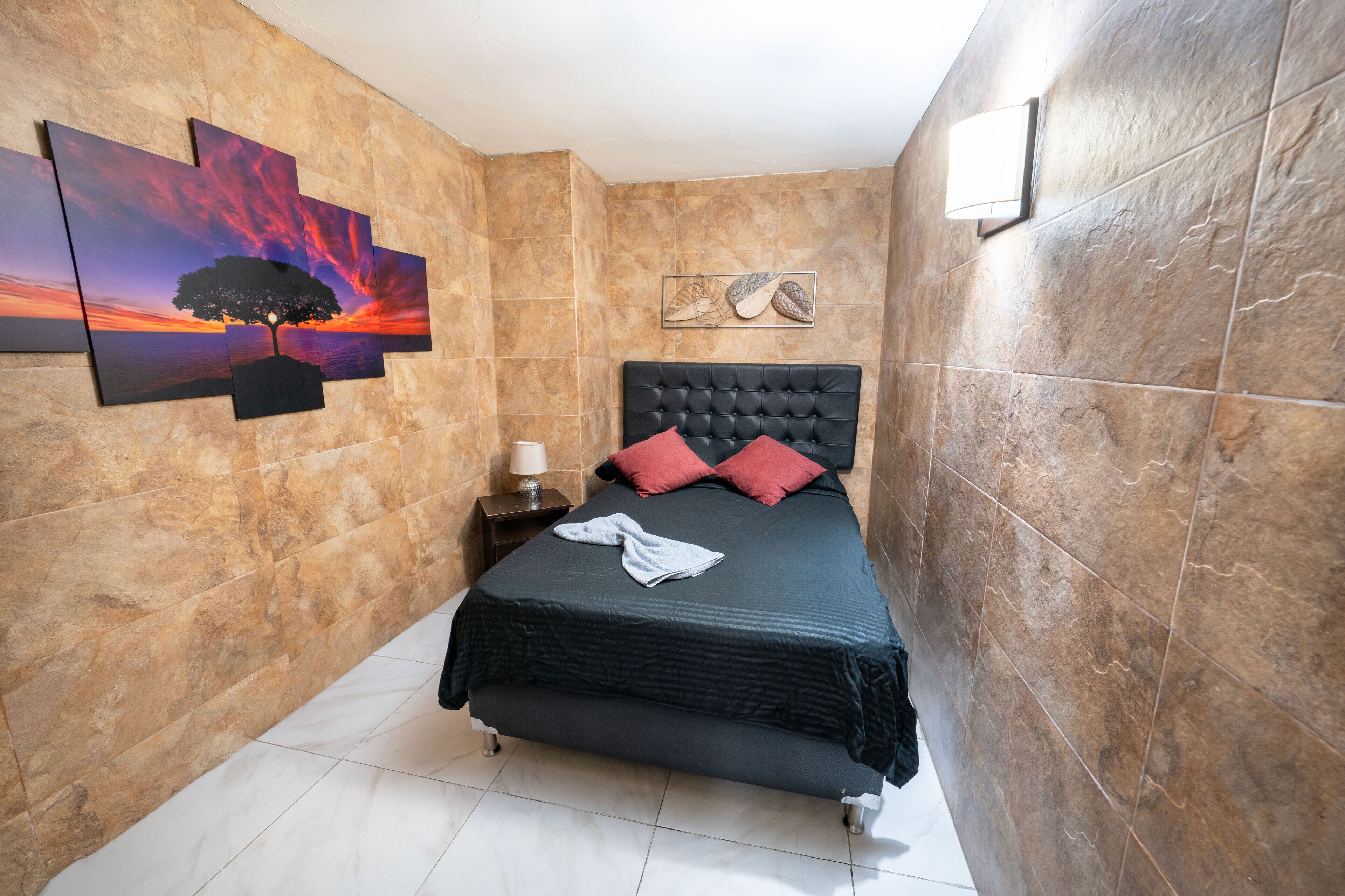 Un dormitorio con una cama, una mesita de noche, una lámpara de pared y obras de arte en la pared.
