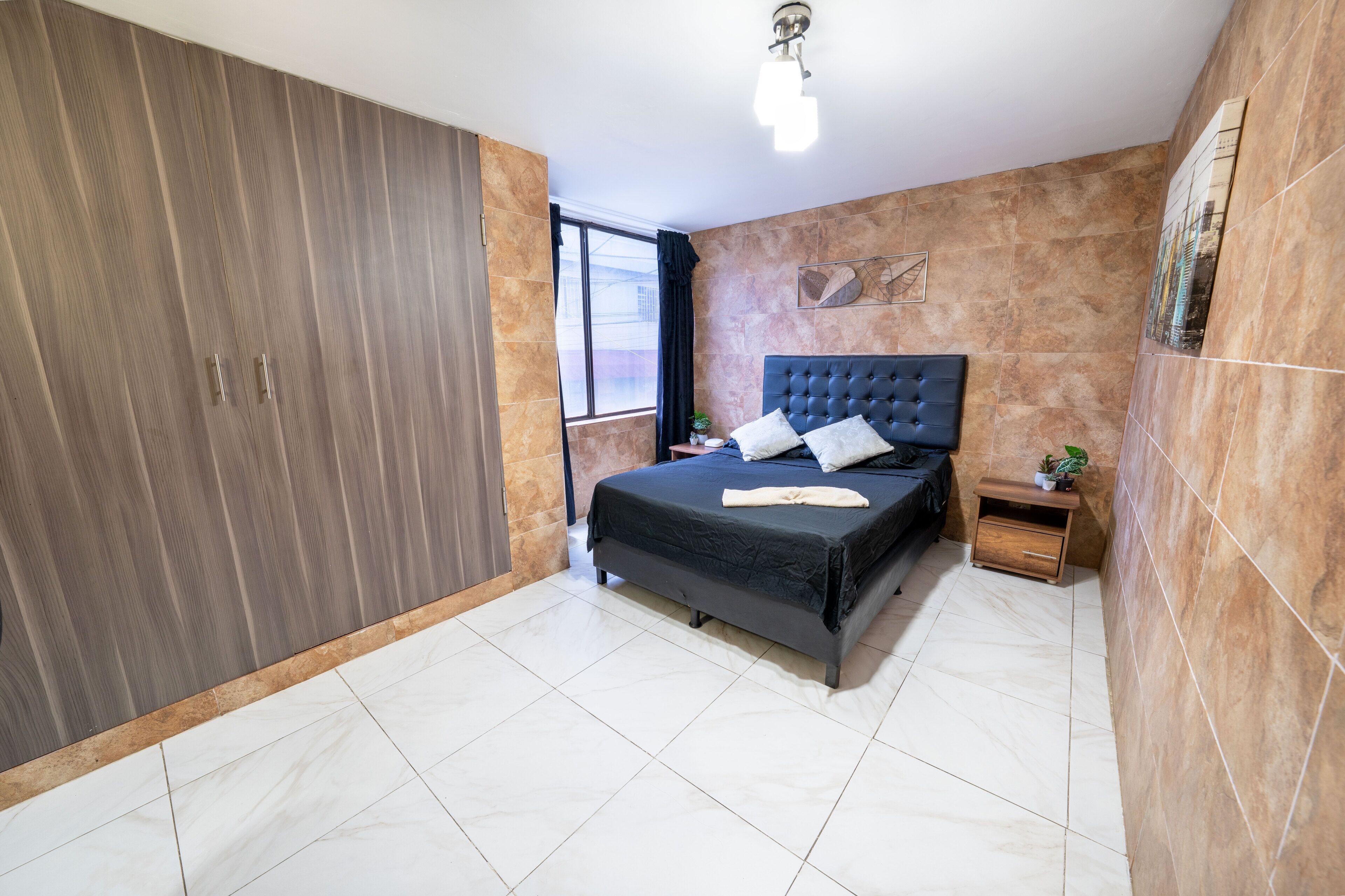 A bedroom with a bed, a wardrobe, a nightstand, and a window.
