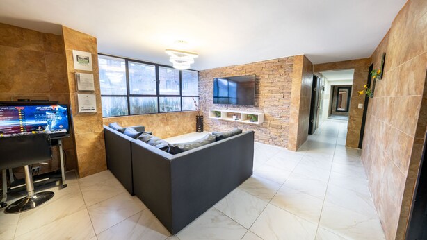 A modern living area with a sofa, a flat-screen TV mounted on a brick wall, a bar area with a TV, and a large window providing natural light. - 5 Bedroom - 1 Block from Lleras - P2 (Medellín)