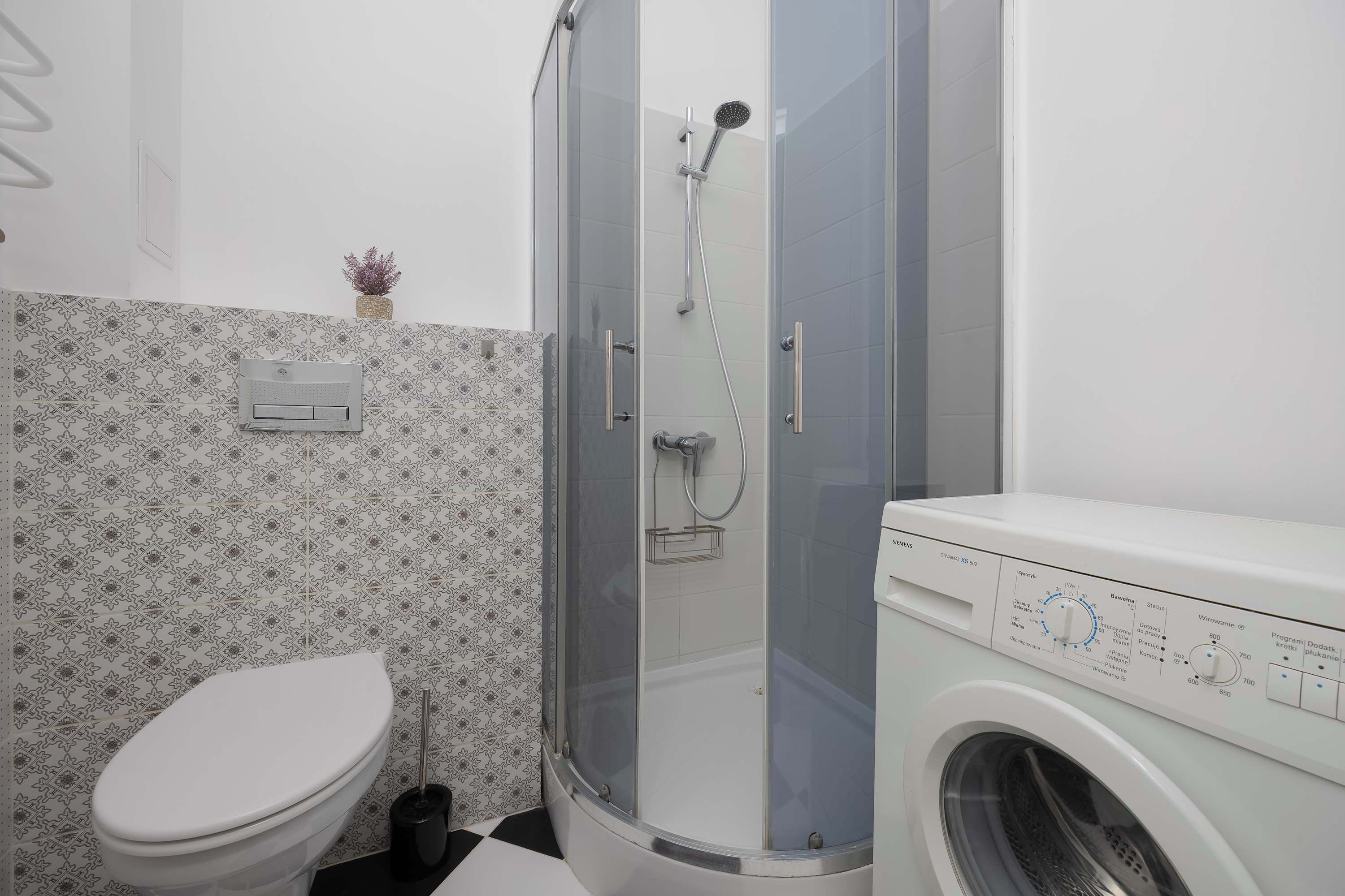 A bathroom with a toilet, a glass-enclosed shower, and a front-loading washing machine.