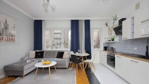 A modern apartment with a grey sofa, a dining table, and a kitchen area with white cabinets and a black countertop. - Apartment with Balcony in the Center | Air Conditioning and View (Warszawa)