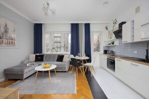 Eine moderne Wohnung mit grauem Sofa, einem Esstisch und einer Küchenzeile mit weißen Schränken und einer schwarzen Arbeitsplatte.