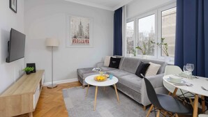 A modern living room with a grey sofa, a white coffee table, and a dining area with a white table and chairs. - Apartment with Balcony in the Center | Air Conditioning and View (Warszawa)