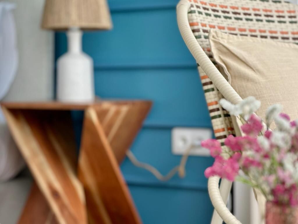 Una silla de mimbre con un cojín, una mesita de madera y una lámpara.