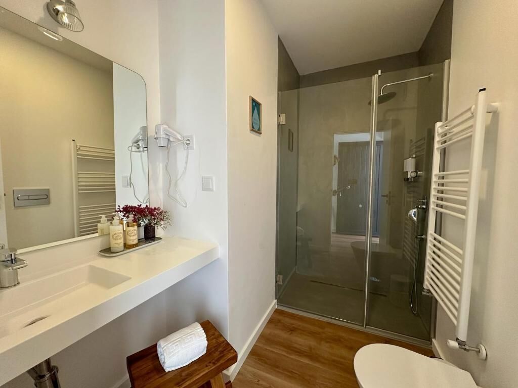 Une salle de bain moderne avec une douche à parois de verre, un lavabo blanc et un banc en bois.
