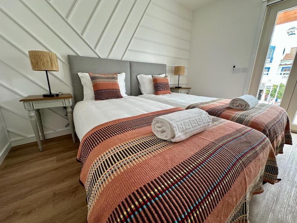 A hotel room with two beds, a wooden floor, and a view of the outside.