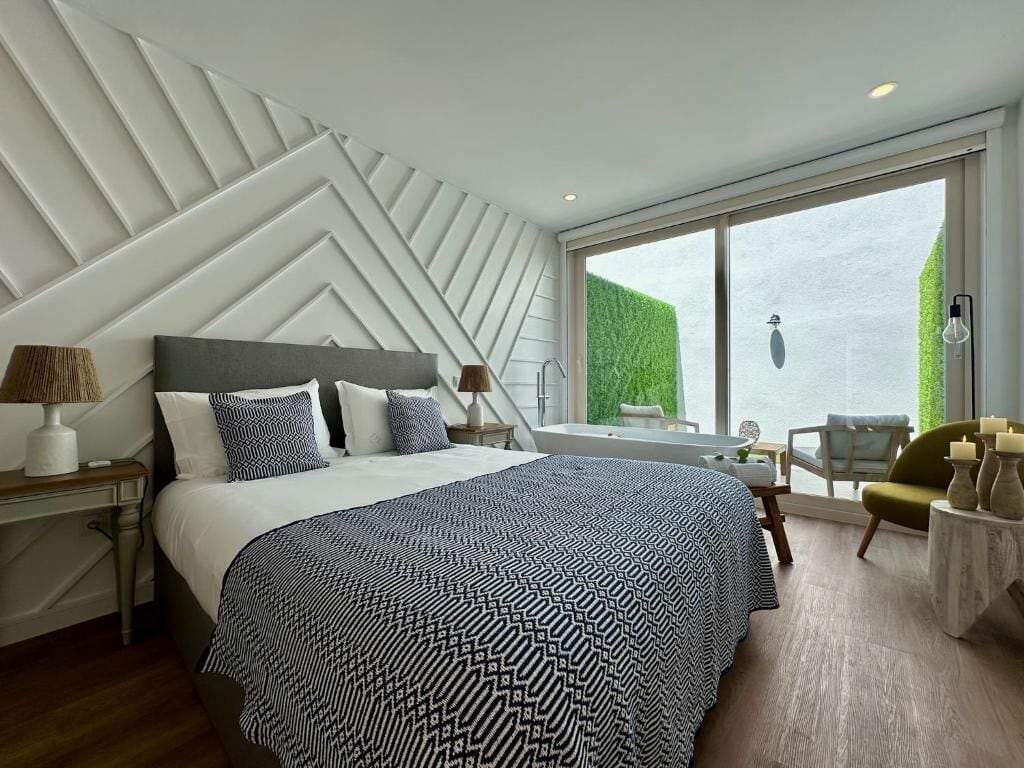 A modern hotel room with a large bed, a view of the sea, and a dining area with a table and chairs.