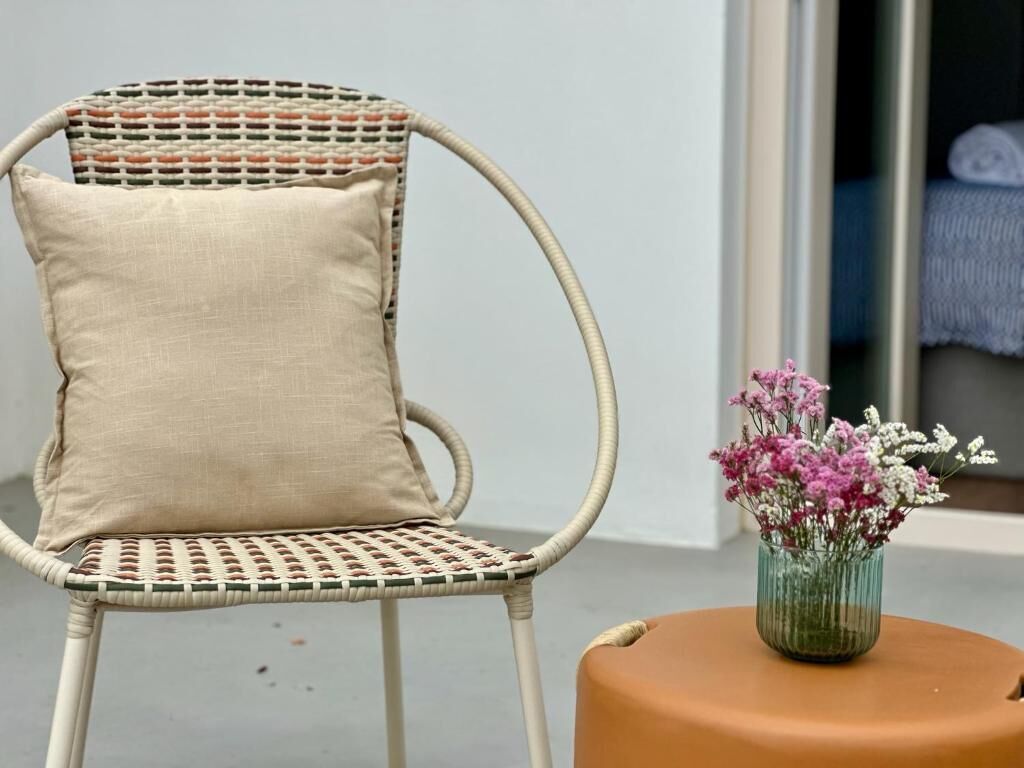 A wicker chair with a beige cushion and a small round table with a vase of flowers.