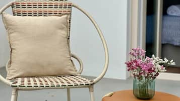 A wicker chair with a beige cushion and a small round table with a vase of flowers.