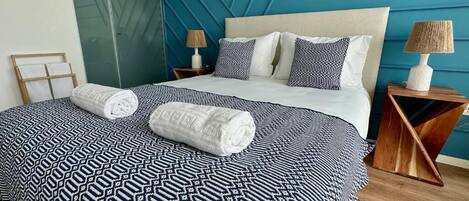 A bedroom with a patterned bedspread, a large bed, two bedside tables with lamps, and a mirror.