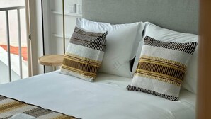 Una cama con sábanas blancas y dos almohadas a rayas.