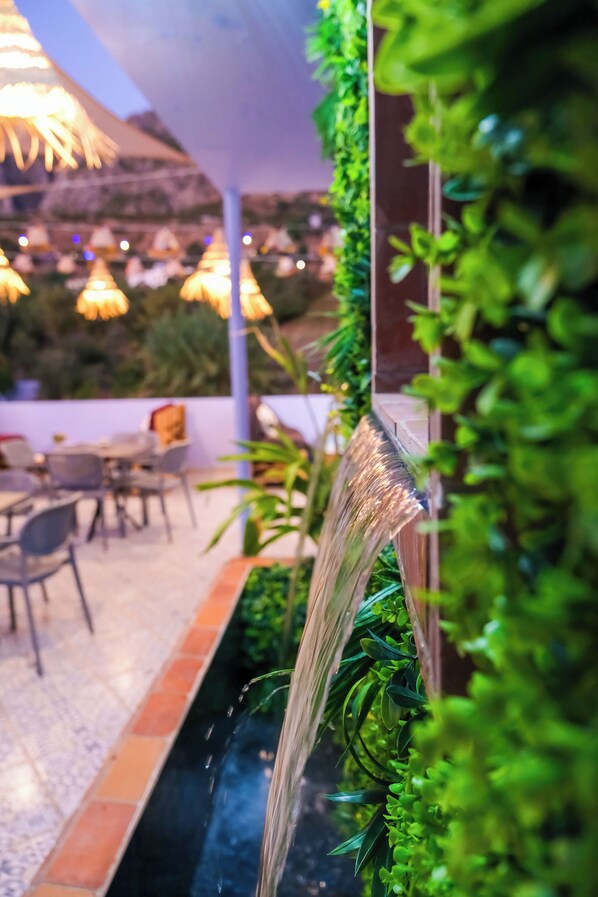 A restaurant patio with outdoor seating, a water feature, and hanging lights.