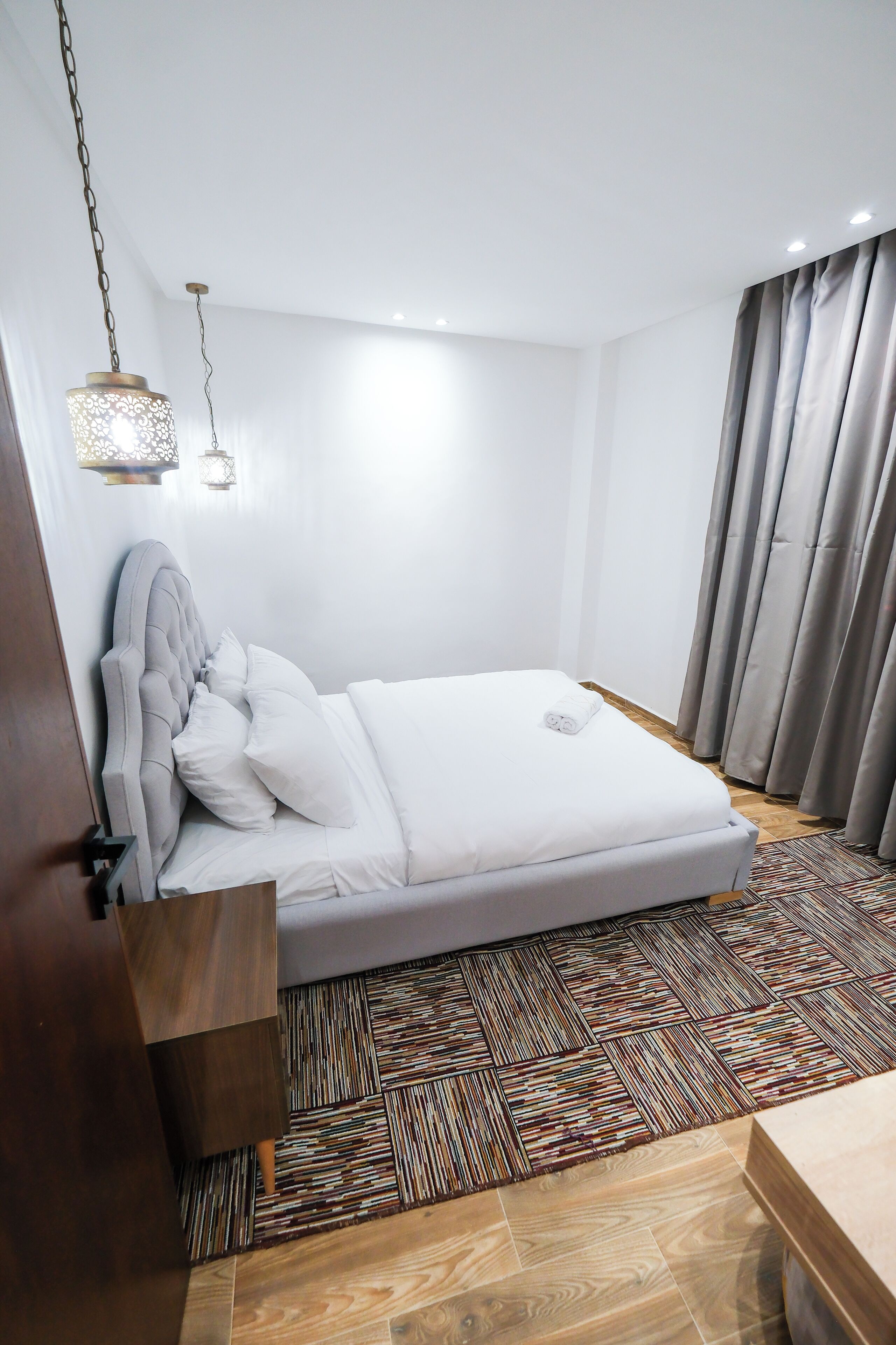 A neatly made bed with a headboard, a patterned rug, and a wooden nightstand.