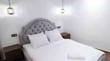 Una cama bien hecha con sábanas blancas, un cabecero capitonado y una mesita de noche con una lámpara.