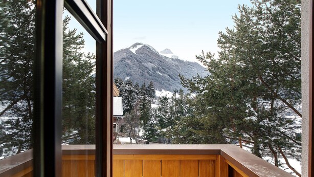 Een houten balkon met uitzicht op besneeuwde bomen en bergen.
