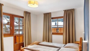 Een slaapkamer met een houten bed, twee ramen met gordijnen, een houten vloer en uitzicht op een besneeerd landschap.