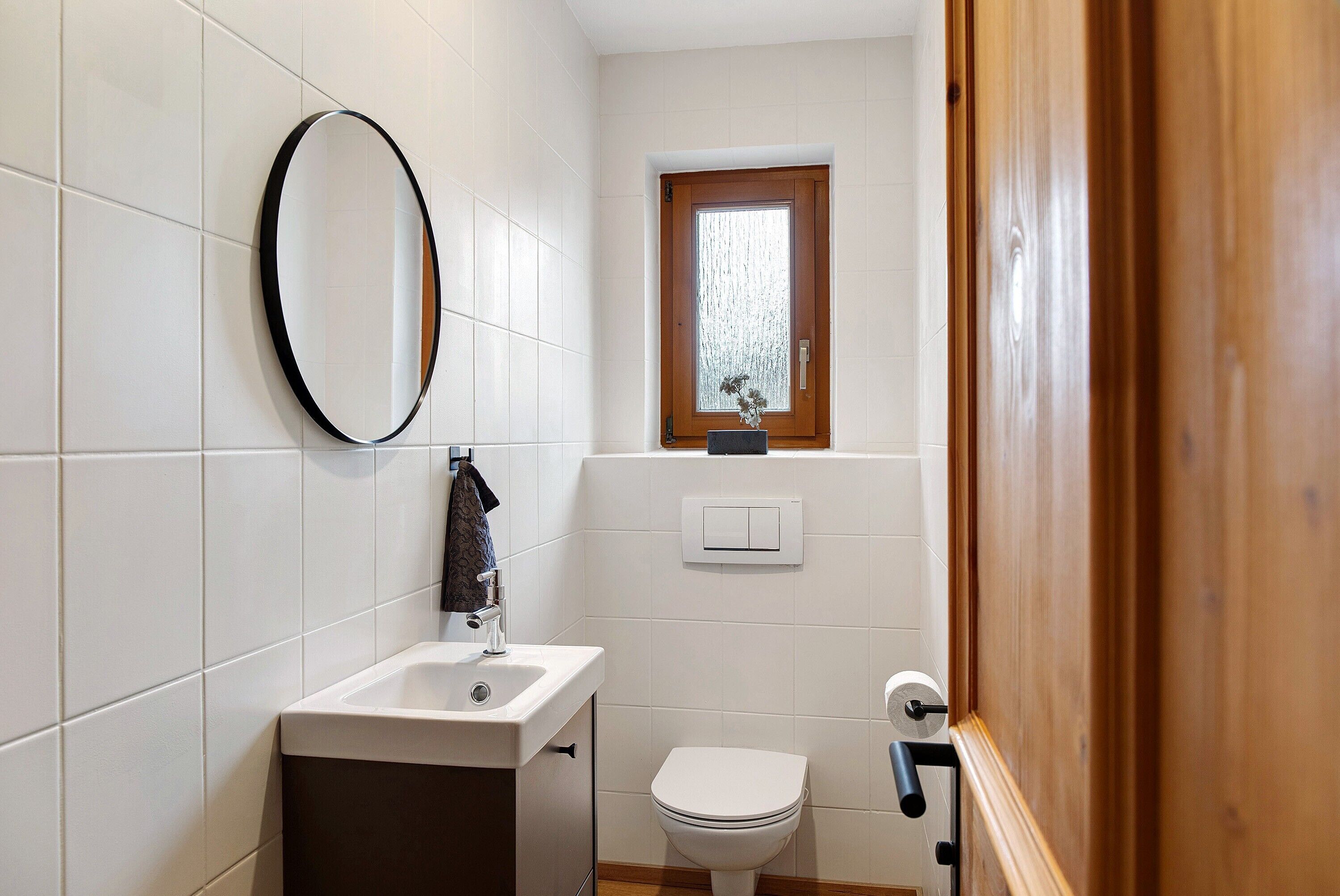 A bathroom with a sink, toilet, mirror, and a window.