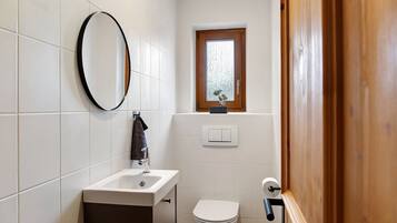A bathroom with a sink, toilet, mirror, and a window.