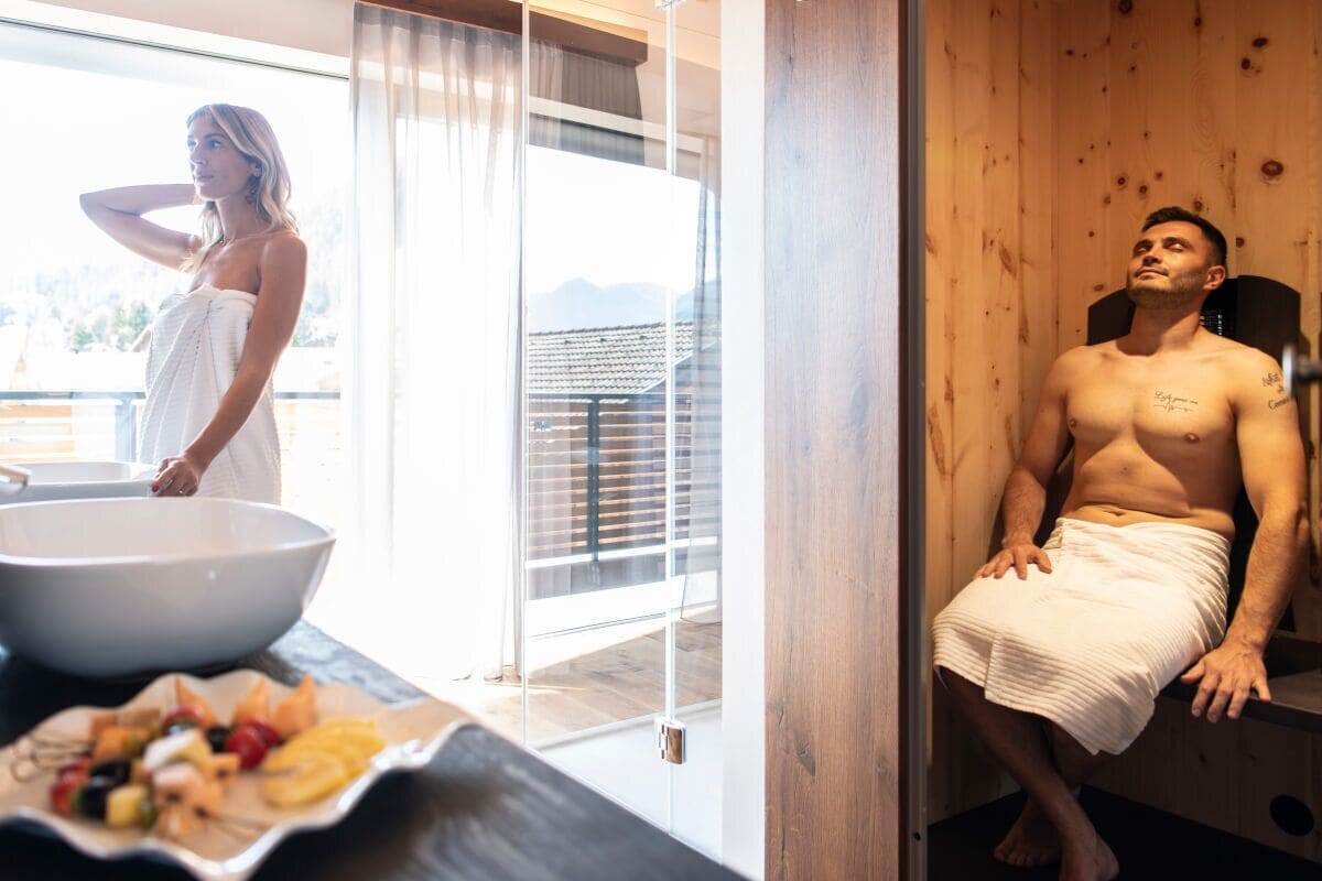 A room with a wooden sauna, a large window with a view of mountains, and a bowl of fruit on the counter.
