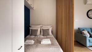A modern bedroom with a neatly made bed, a blue sofa, and a wooden partition.