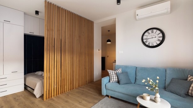 A modern living room with a blue sofa, a small white table, and a wooden partition.