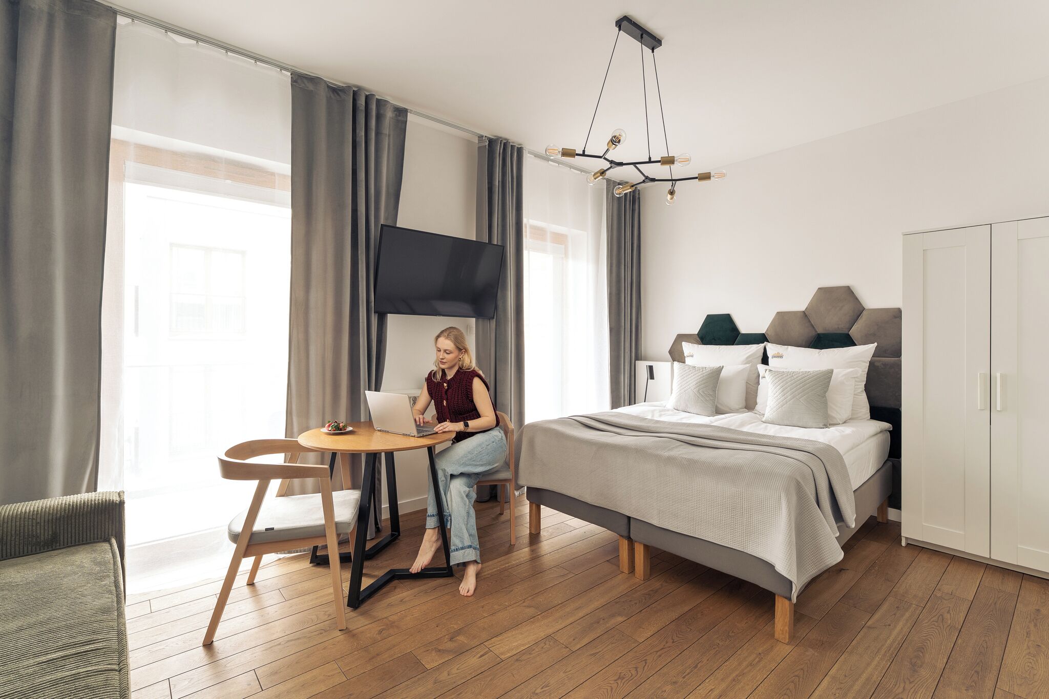 A modern bedroom with a bed, a desk, a chair, a television, and a wardrobe.