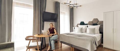 A modern bedroom with a bed, a desk, a chair, a television, and a wardrobe.