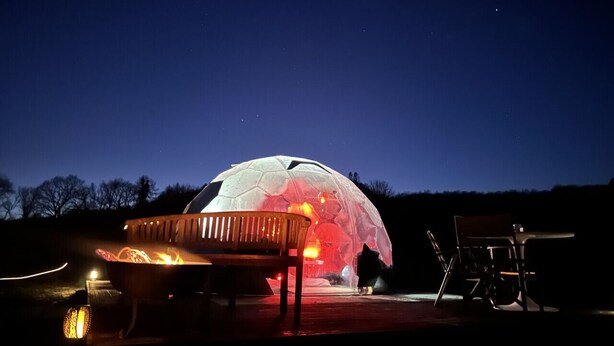 A dome-shaped structure with a fire in the center, surrounded by outdoor seating. - Cosy Off-Grid Stargazing Dome in the Jurassic Coast with optional Hot Tub & Sauna (Devon)