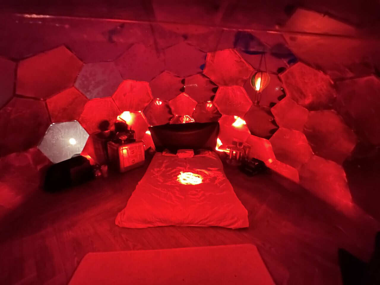 Ein Zimmer mit einer sechseckigen Steinwand, einem Bett mit roter Decke und einer hängenden Laterne.