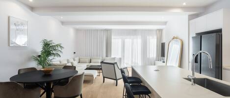 A modern kitchen with a large island, a dining area with a round table and chairs, and a living area with a sofa and chairs.