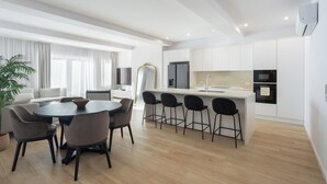 A modern kitchen with white cabinets, a central island with bar stools, and a dining area with a round table and chairs. - Marques DE Pombal Grand Prestige (Lisbon)