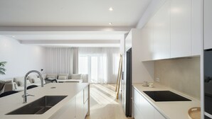 A modern kitchen with white cabinetry, a central island with a sink, and a dining area with a sofa and curtains. - Marques DE Pombal Grand Prestige (Lisbon)
