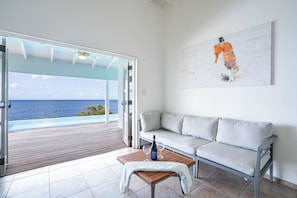 Ein Zimmer mit einem weißen Sofa, einem Holztisch mit Flasche und Gläsern sowie einem Bild an der Wand.