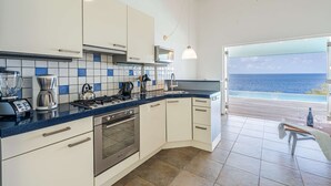 A kitchen with white cabinets, a blue countertop, and a view of the ocean.