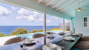 A dining area with a view of the ocean, a pool, and a covered patio.