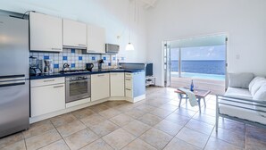 A modern kitchen with white cabinets, a blue countertop, and a view of the sea through a glass door.