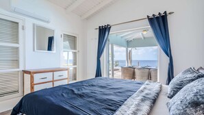 A bedroom with a bed, a dresser, and a view of the sea.