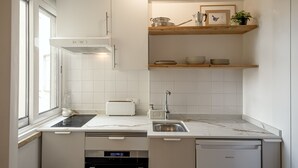 Egy modern konyha fehér szekrényekkel, beépített sütővel, mosogatógéppel és egy ablakkal, amely természetes fényt biztosít.