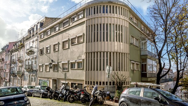 Egy többemeletes épület, amelynek ívelt homlokzata, erkélyei és parkolóban tárolt motorkerékpárjai vannak.