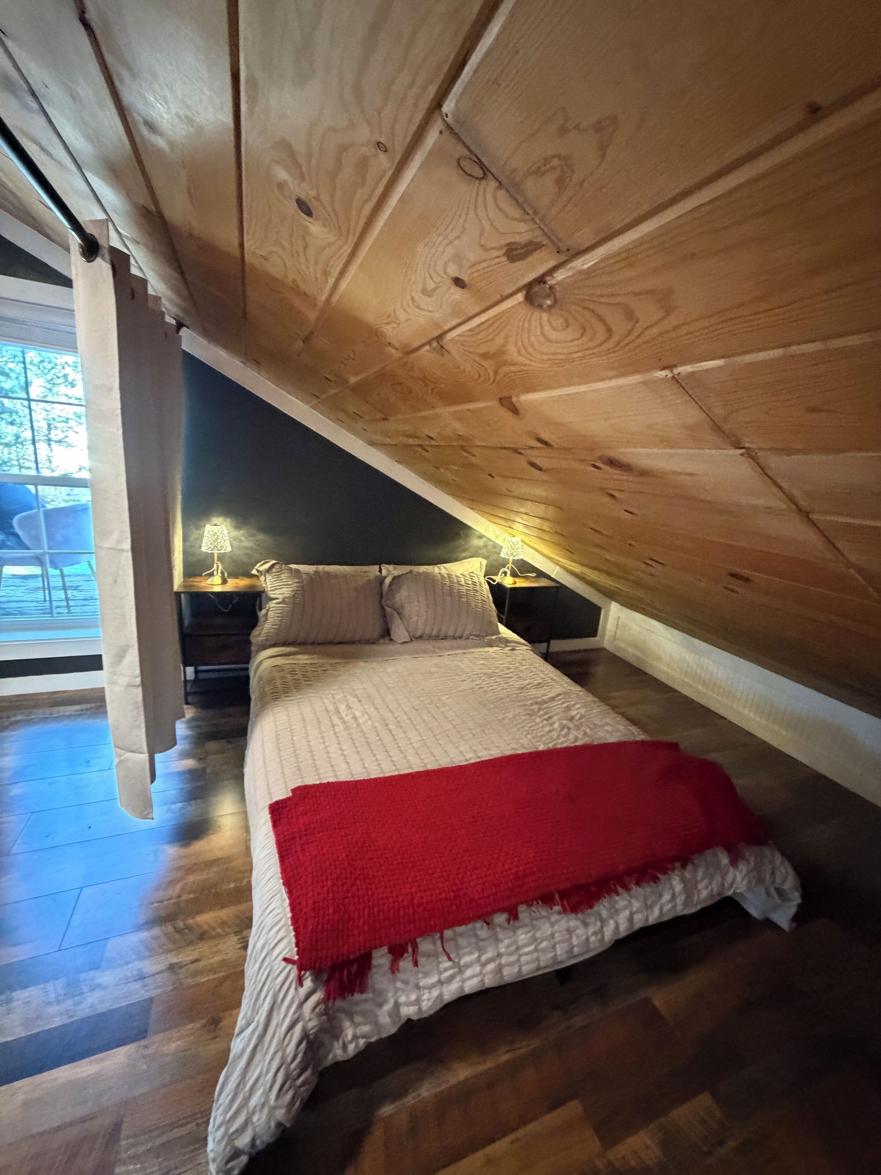Une chambre avec un plafond en pente, un lit recouvert d’une couverture rouge et deux lampes de chevet.