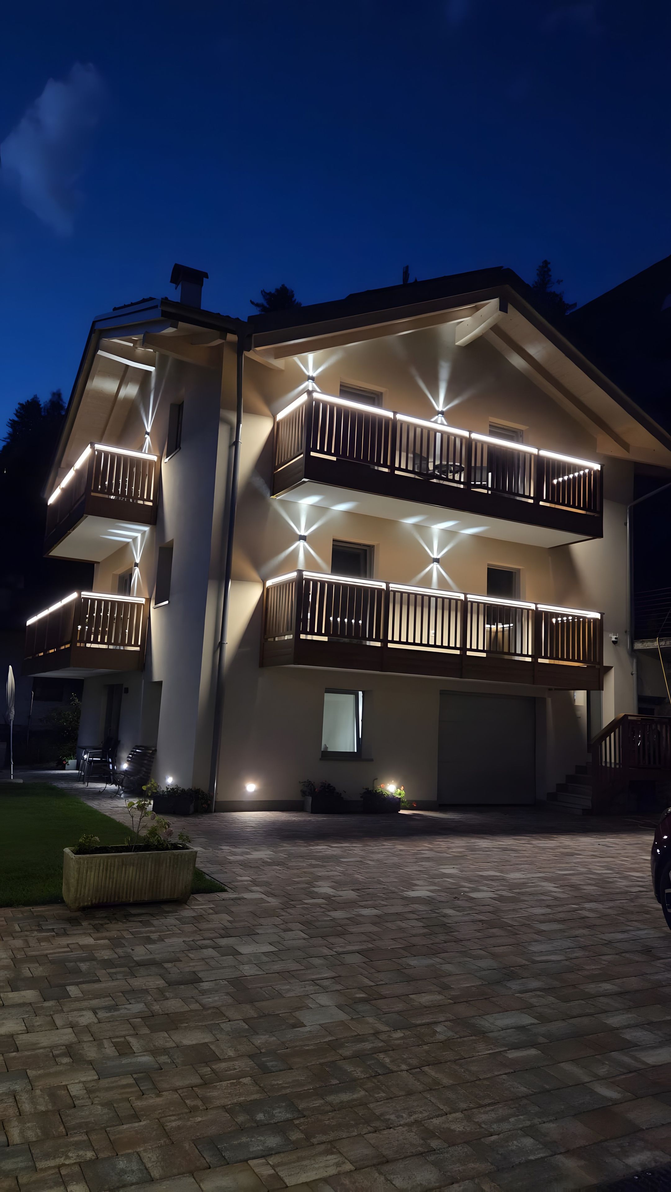 Un immeuble à plusieurs étages, doté de balcons illuminés et d’une allée pavée.