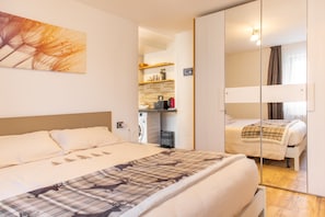 Ein Schlafzimmer mit Bett, Spiegel, Wandbild und einer Küchenzeile.