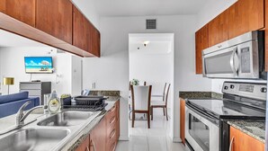 Une cuisine moderne avec des meubles en bois, des appareils en acier inoxydable et un coin repas doté d’un téléviseur diffusant des images d’une plage.
