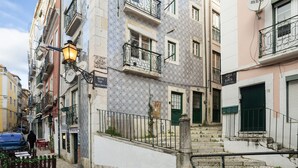 Une rue étroite bordée d’immeubles aux façades ornées de carreaux de céramique traditionnels portugais, avec une chaussée pavée et une rambarde métallique le long du trottoir.