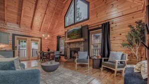 A spacious log cabin interior with a stone fireplace, wooden furniture, and large windows. - *Spacious 5BD Lodge w/ VIEWS | Theater + Hot Tub* (Sevierville)