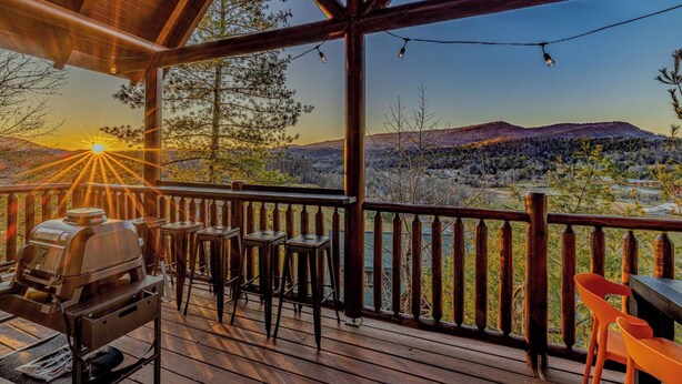 A wooden deck with a barbecue grill, bar stools, and a table, overlooking a mountainous landscape. - *Spacious 5BD Lodge w/ VIEWS | Theater + Hot Tub* (Sevierville)