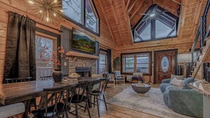 A spacious wooden cabin with a dining area, a living room with a sofa, and a fireplace. - *Spacious 5BD Lodge w/ VIEWS | Theater + Hot Tub* (Sevierville)