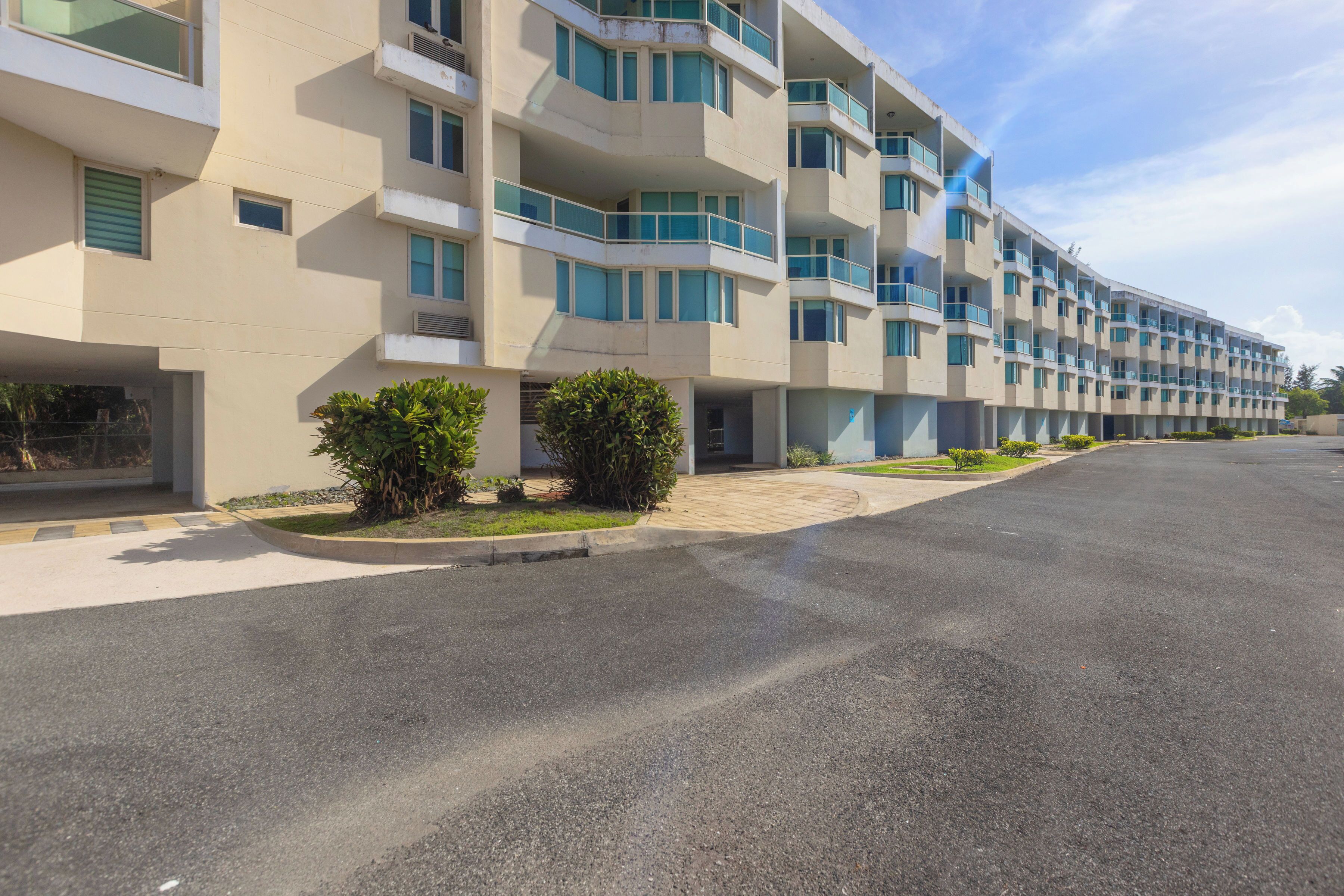 Un hôtel à plusieurs étages au design moderne, doté de balcons à chaque étage, d’une allée pavée et de petits espaces paysagers agrémentés d’arbustes.